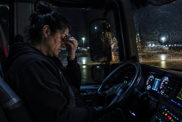 Motorista exausta dentro da cabine do caminhão à noite esfregando os olhos