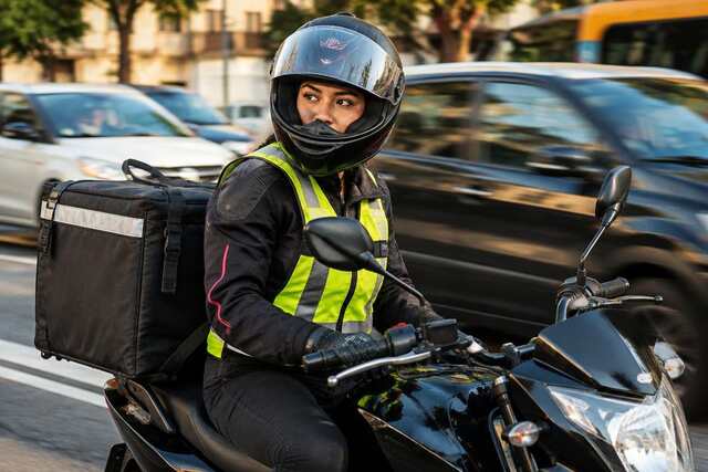 Motociclista de entregas com capacete e colete refletivo no trânsito urbano