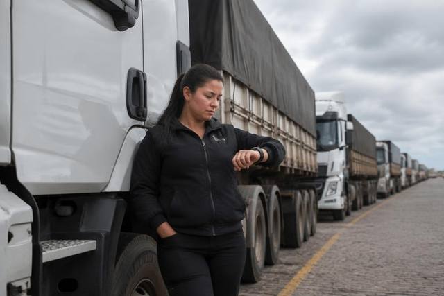 Motorista olhando o relógio encostada no caminhão em fila de pátio de carregamento